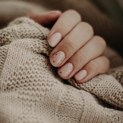 Photo by Kristina Paukshtite Close-up of a hand with polka dot manicured nails wrapped in a knitted sweater.